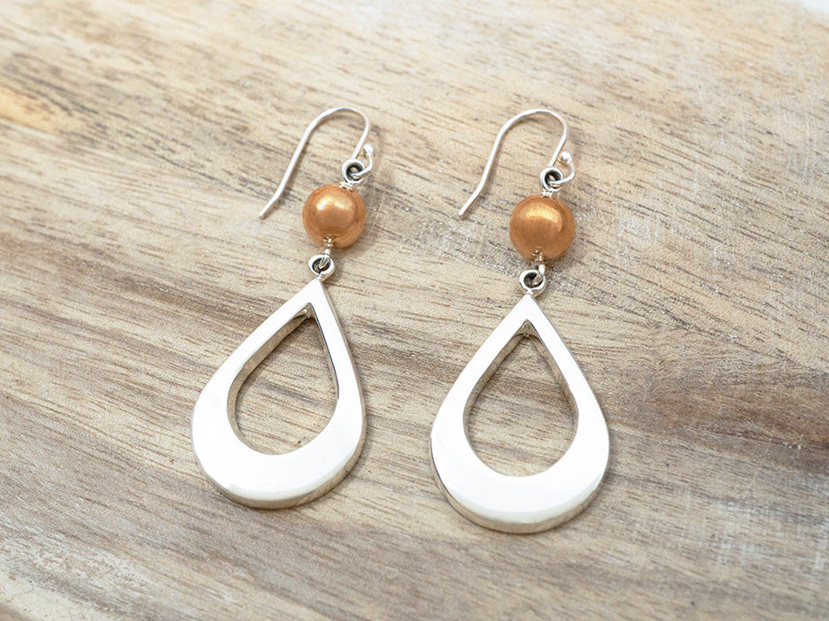 A pair of earrings featuring a silver teardrop hanging from a copper bead on a sterling silver hook.