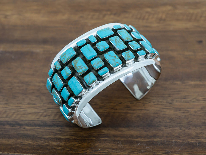 Wide sterling silver cuff with turquoise stones laid out in a cobblestone pattern. 