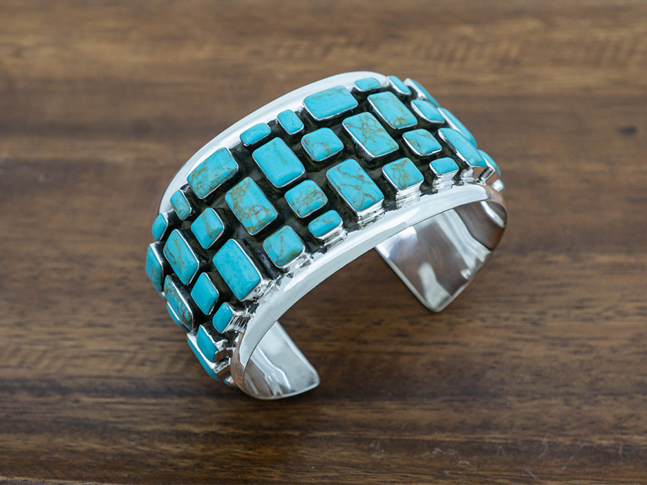 Wide sterling silver cuff with turquoise stones laid out in a cobblestone pattern. 