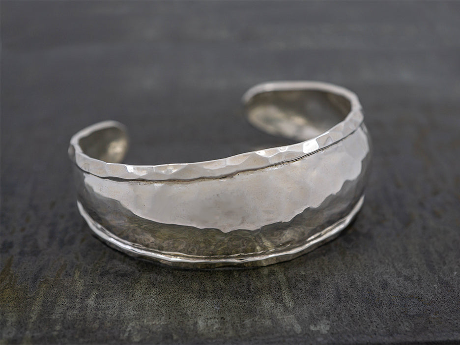 A hammered sterling silver cuff bracelet with a frame around the edge.