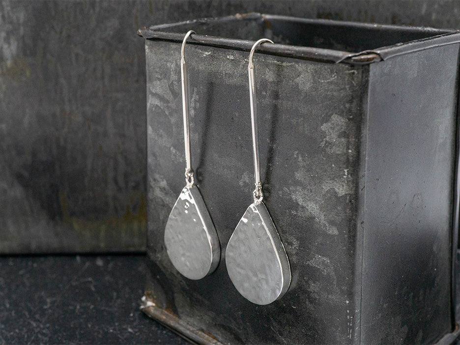 a hammered, hollow, teardrop earring on a long drop made of sterling silver.