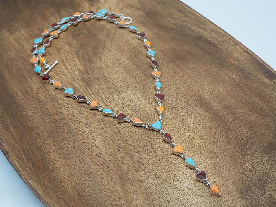 A sterling silver lariat necklace made with multicolored stones cut into trillions and teardrops.
