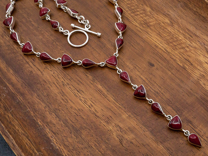 A sterling silver lariat necklace made with teardrop and trillion cut red jasper stones. The necklace has a toggle closure..