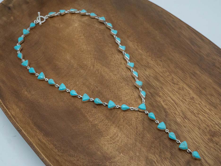 A sterling silver lariat necklace made with turquoise stones cut into teardrop and trillion shapes.
